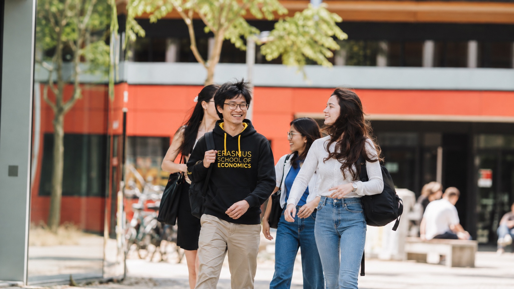Four students walking and talking outside a campus building on a summer day, one in an Erasmus School of Economics hoodie